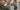 Hand holding a metal watering can in front of a garden or roses