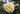 A close-up of a ruffled rose in bloom with pale yellow and creamy white petals, alongside a closed bud, set against a soft-focus green garden background.
