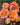 A close-up of a hand holding a cluster of blooming roses with peach, orange, and pink petals, set against a background of green garden foliage.