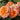 A close-up of peach and pink rose blooms with green leaves growing in a garden bed.