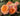 A close-up of peach and pink rose blooms with green leaves growing in a garden bed.