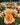 Close-up of peach and yellow roses with green leaves in a garden bed, with more roses blurred in the background.