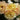 Close-up of pale yellow and peach roses with ruffled petals and dark green foliage in the background.