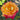 A close-up of a blooming rose with layered petals that fade from bright yellow-orange in the center to deep pink and red at the edges, surrounded by green leaves and a softly blurred outdoor background.