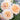 Close-up of three delicate peach-colored roses with green leaves and purple flowers in the background