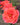 A close-up photograph of a vibrant coral-pink rose in full bloom, with other blurred roses and green foliage in the background.