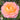 A single peach-pink rose bloom with a yellow-orange center, photographed in a garden with green leaves and blurred foliage in the background.