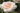 A close-up of a pale blush pink rose in full bloom, with soft layered petals and a softly blurred green garden background.